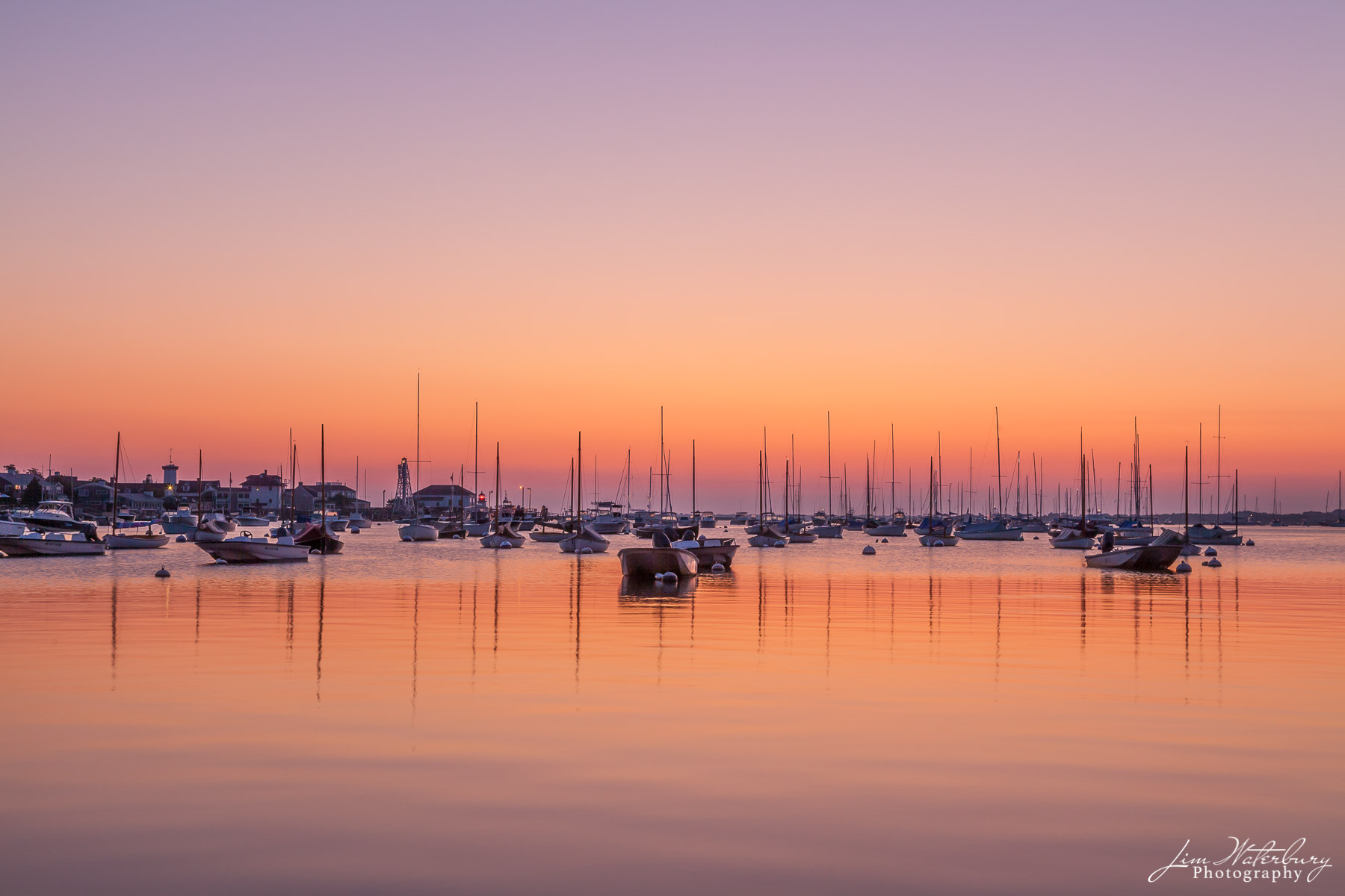 Boats at dawn in Nantucket Harbor under a pink and purple cloudless sky.