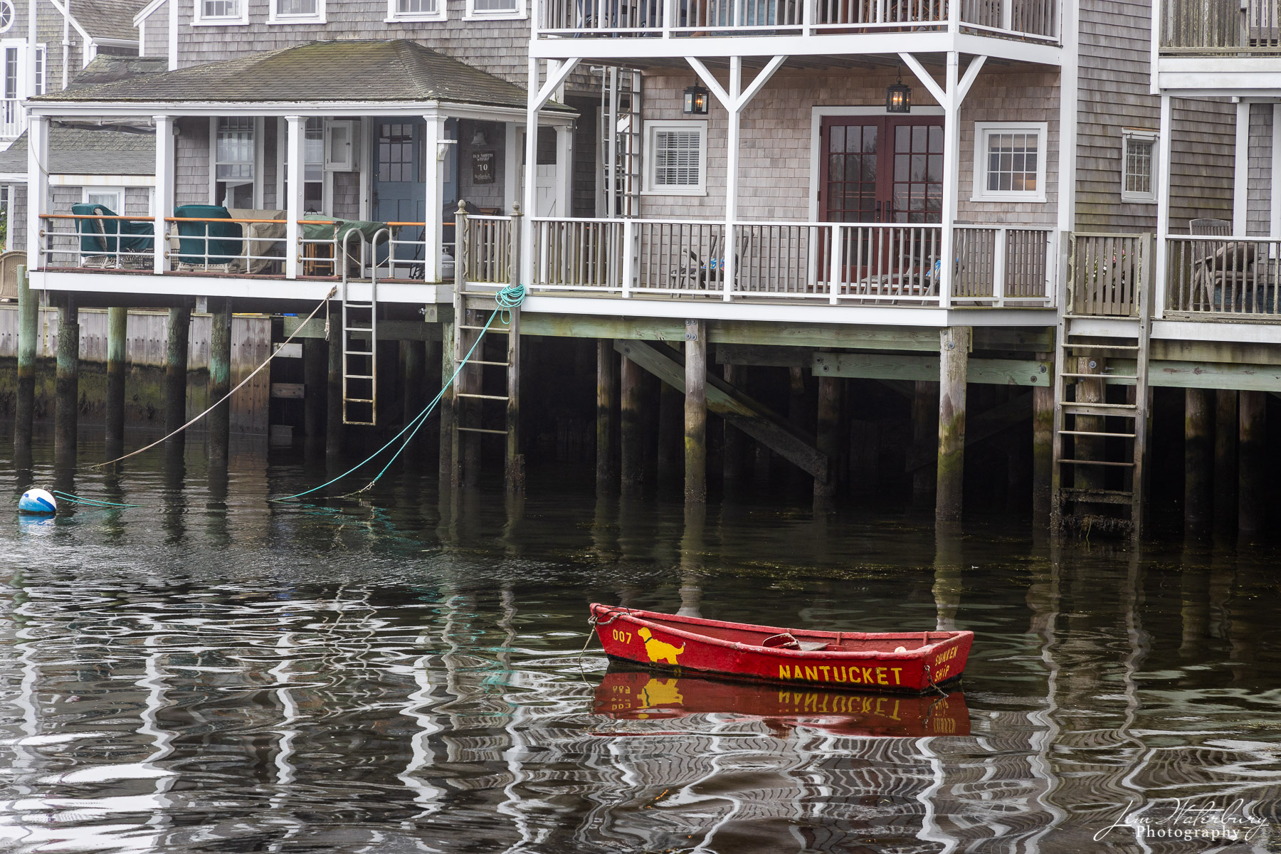 The Sunken Ship's classic red dinghy sits in the water among the geometric reflections of the Old North Wharf cottages on Easy...