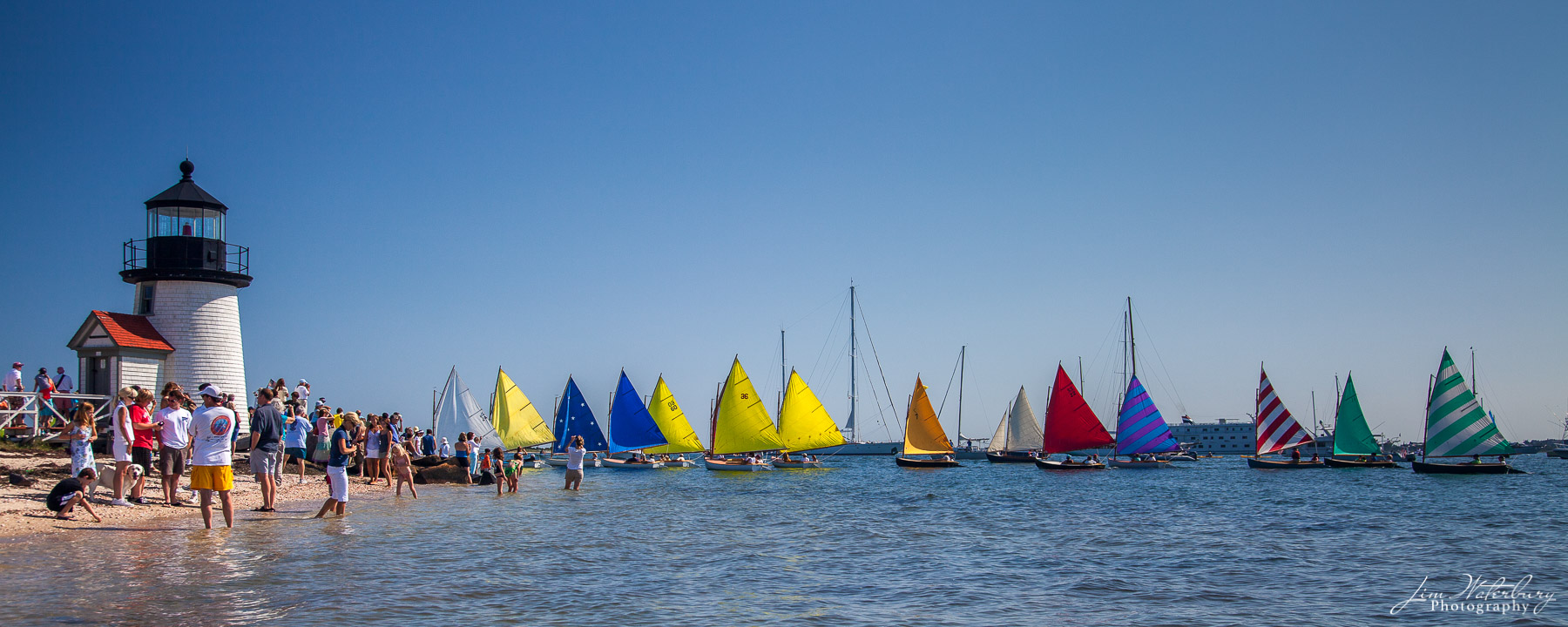 Rounding Brant Point Parade of the Rainbow Fleet, with their colorful sails, around Brant Point Lighthouse, Nantucket, during Race Week.