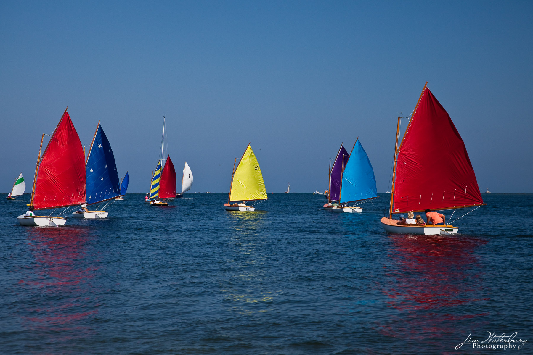 The Nantucket Rainbow fleet, with their colorful sails, parade past Brant Point Lighthouse to mark the beginning of the day of...