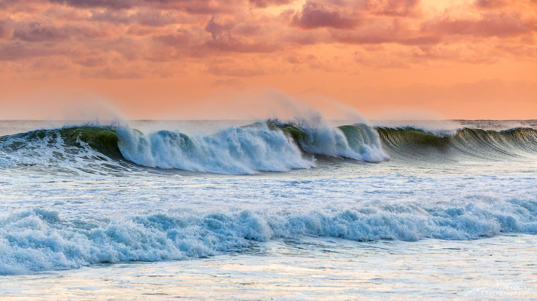 A line of waves crashes to the beach on Nantucket's south shore under an orange sky