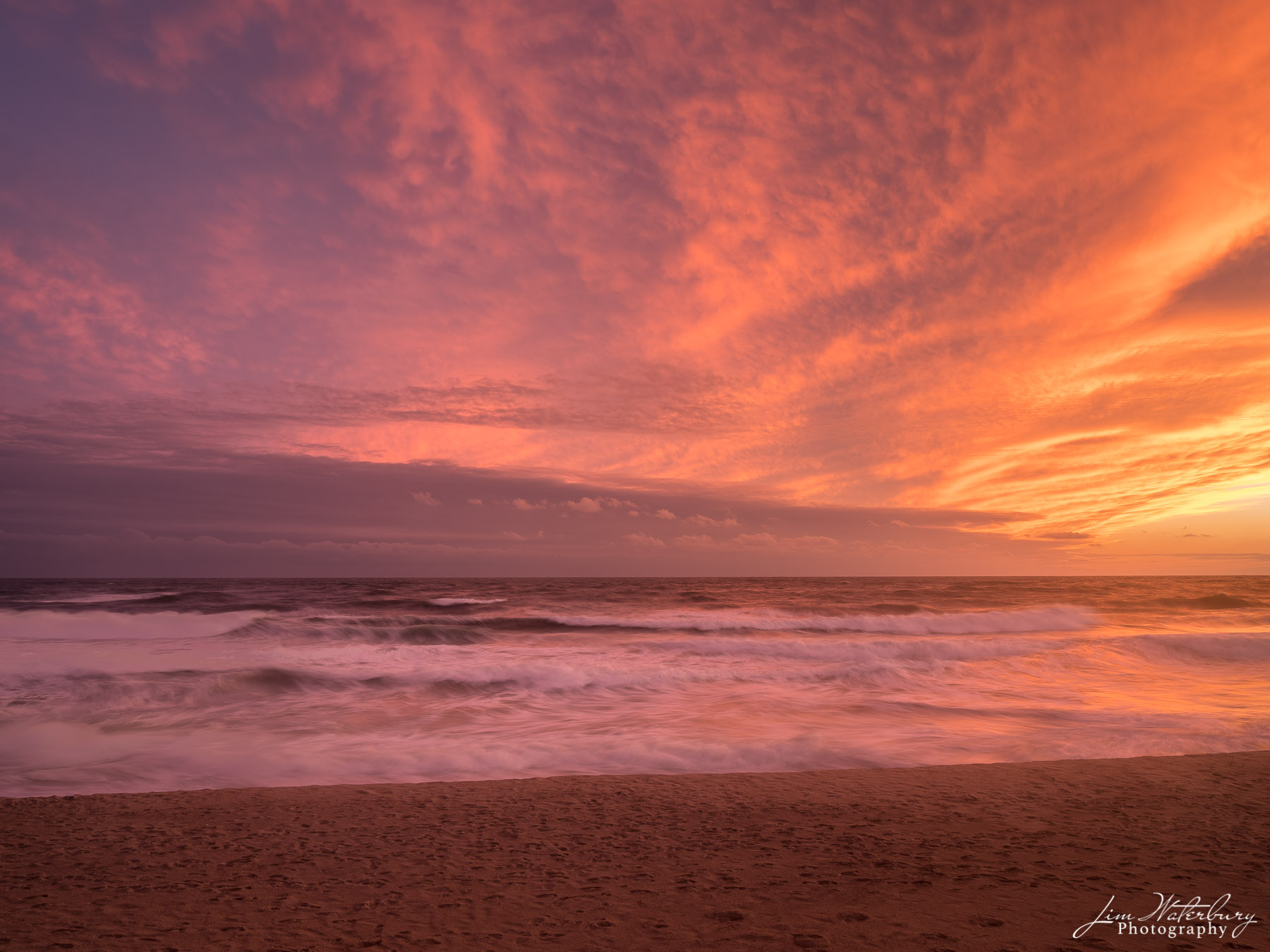 A late fall sunset produces a fiery orange and pink sky, reflecting off the surf of the Atlantic Ocean.