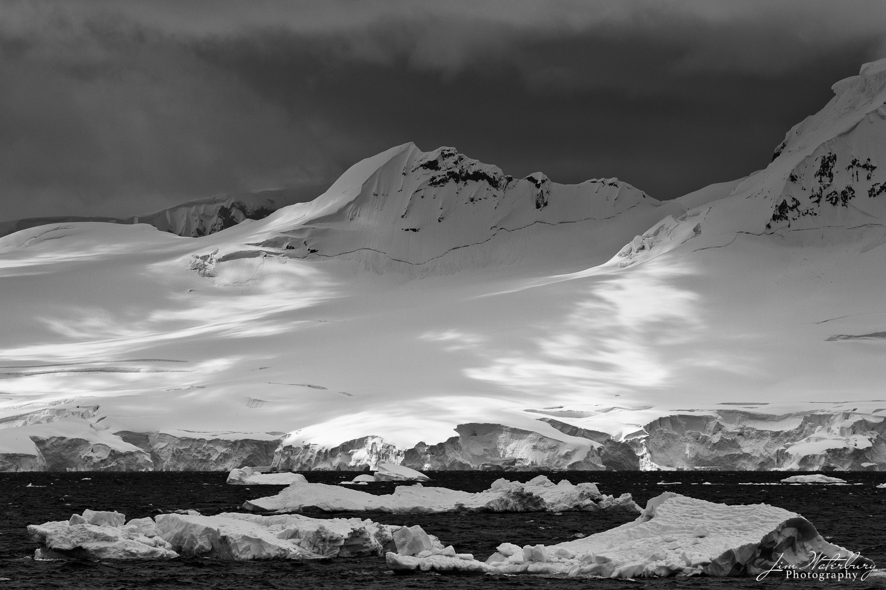 Light and shadows play on snow-covered mountains in the Antarctic Peninsula in this black & white image.