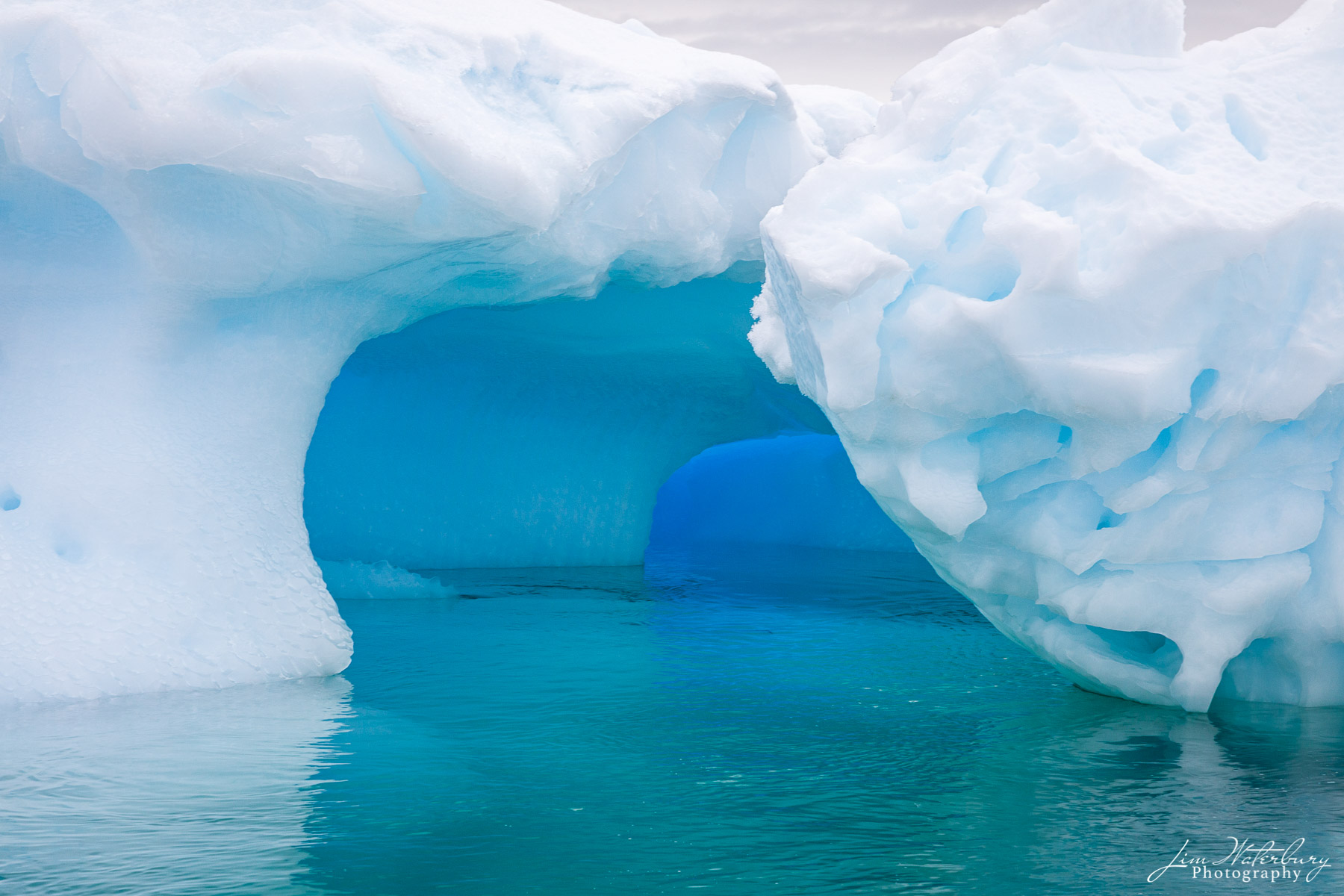 Ice Tunnel A tunnel, formed on the bottom of an iceberg floating in the Lemaire Channel, shows striking shades of aqua and blue -- in the...