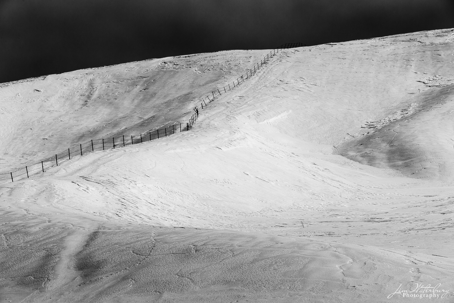 Black & white image of a steep, snow-covered hill in Hokkaido, Japan, divided in half by a wooden fence.