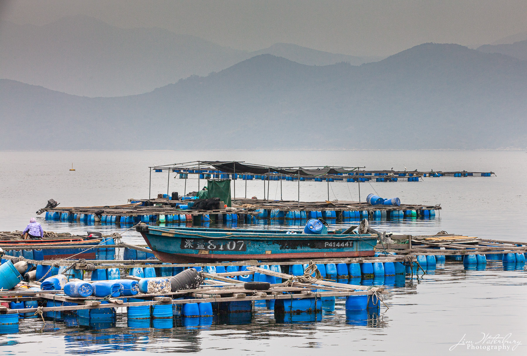 Blue Daze A floating fish farm at Tap Mun (Grass Island), Hong Kong, against a backdrop of hazy mountains in the distance. Tap Mun is located...