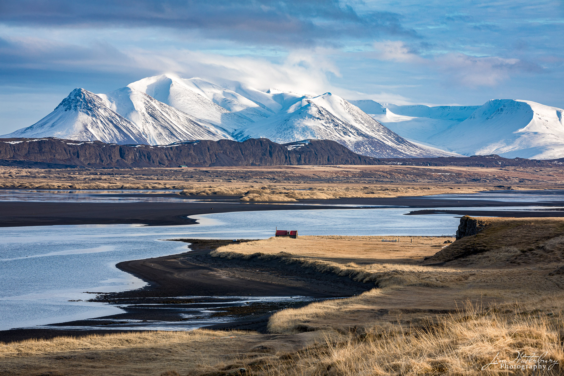 A collection of snow-covered mountains, golden plains, black sand beaches, and the blue waters of a fjord paint a landscape very...