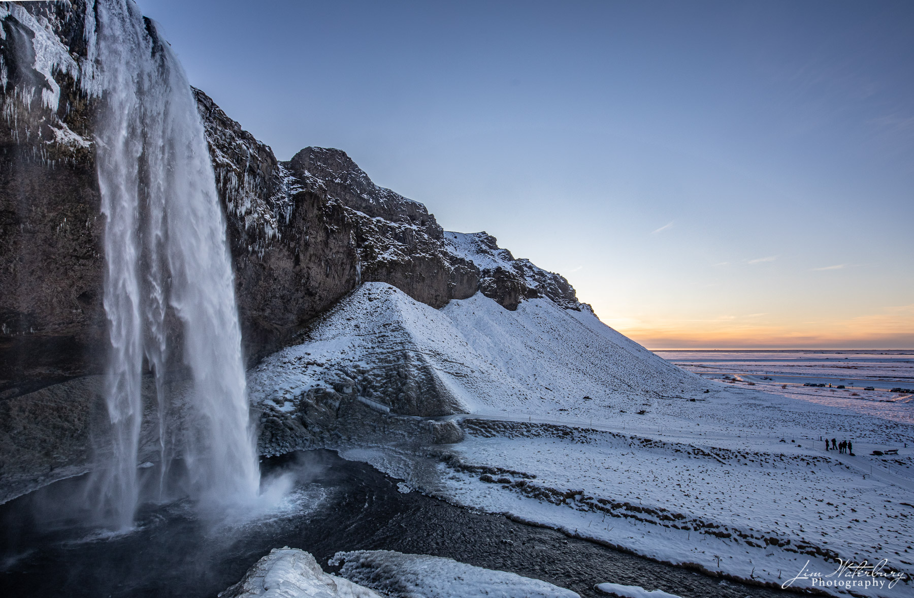 Seljalandsfoss waterfall accents a snow-covered winter landscape in Southern Iceland at sunset.