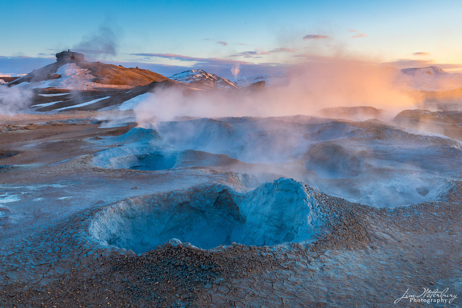 The soft, warm light of sunrise illuminates the smoking fumaroles and blue-rimmed boiling mud pots of the Namaskard geothermal...