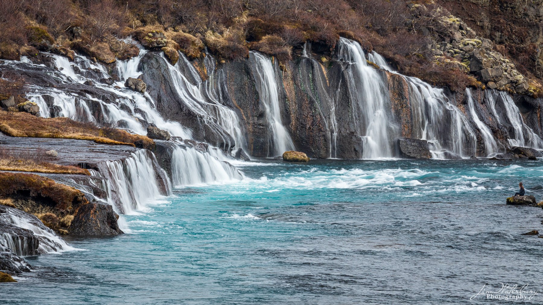 Cascading Glacier A young girl sits on an outcrop of rock to take in the natural beauty of the Hraunfossar waterfalls, as glacial melt waters cascade...