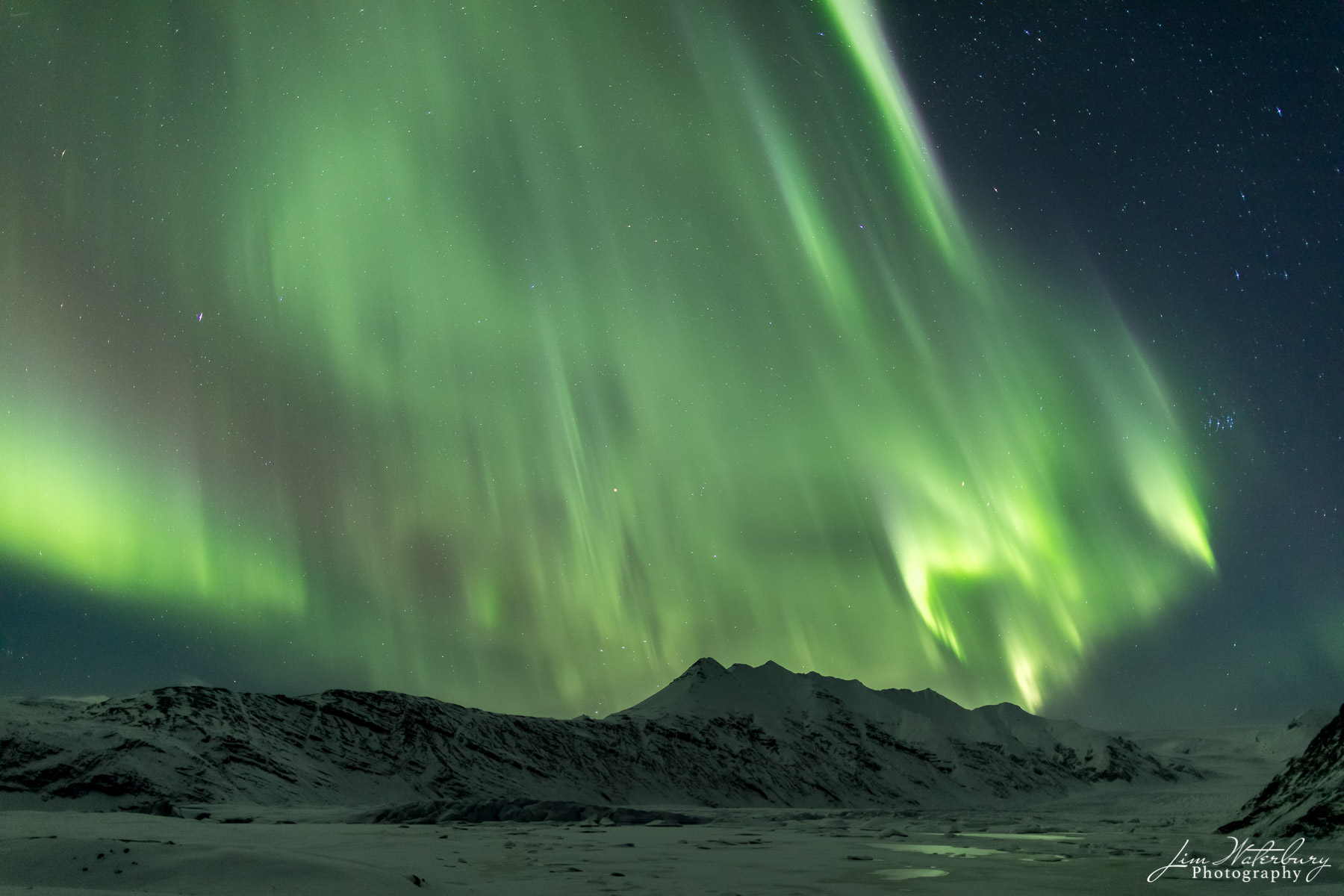 Northern lights (Aurora Borealis) dance in a star-studded sky above the mountains and frozen tundra of Iceland.