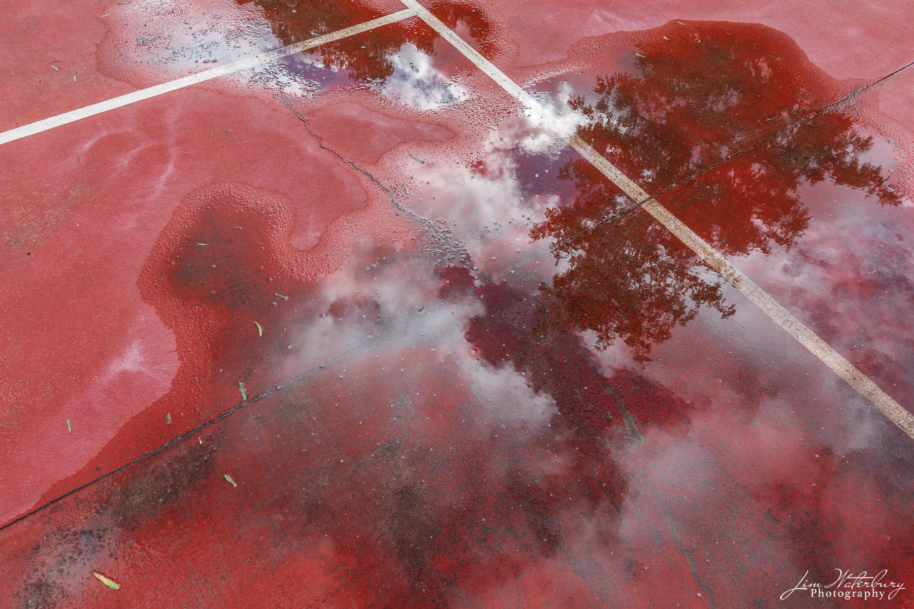 Sky and clouds reflect in rain puddles on a red, hard tennis court at a hacienda outside San Miguel de Allende, Mexico