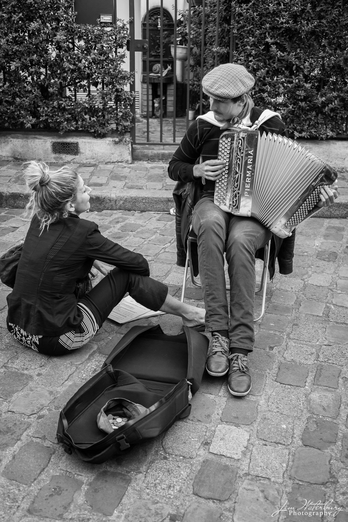 An accordian player performs for a fan on the streets of Montmartre, Paris.  Black & white.