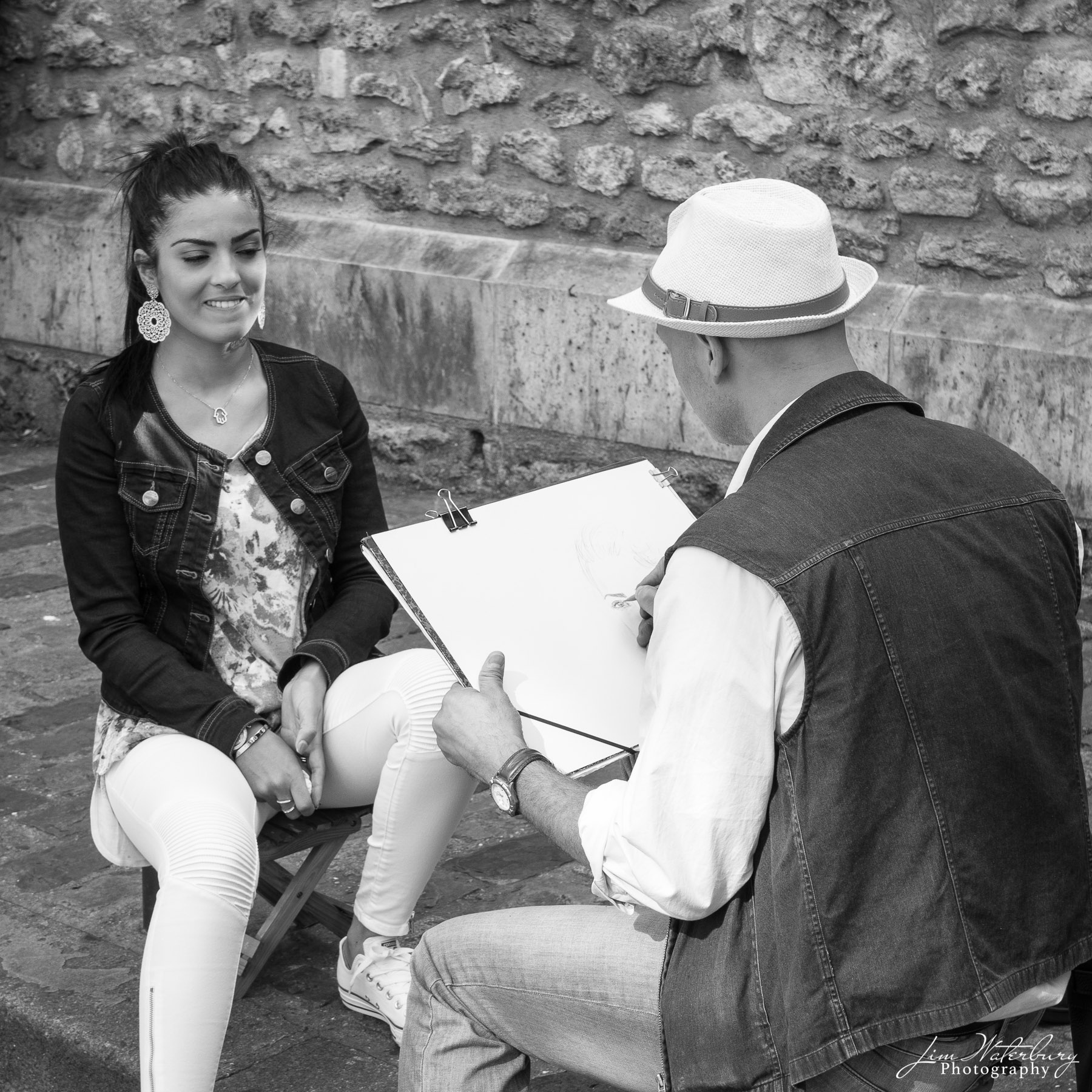 The Portrait Artist in Montmartre, Paris, begins a charcoal drawing of a young woman. Black & white.