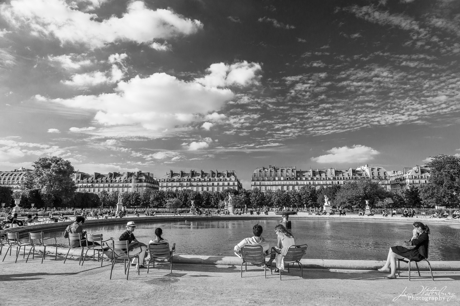 Parisiens and tourists enjoy a warm June day around the pond in the Tuileries garden in Paris.  Black & white.