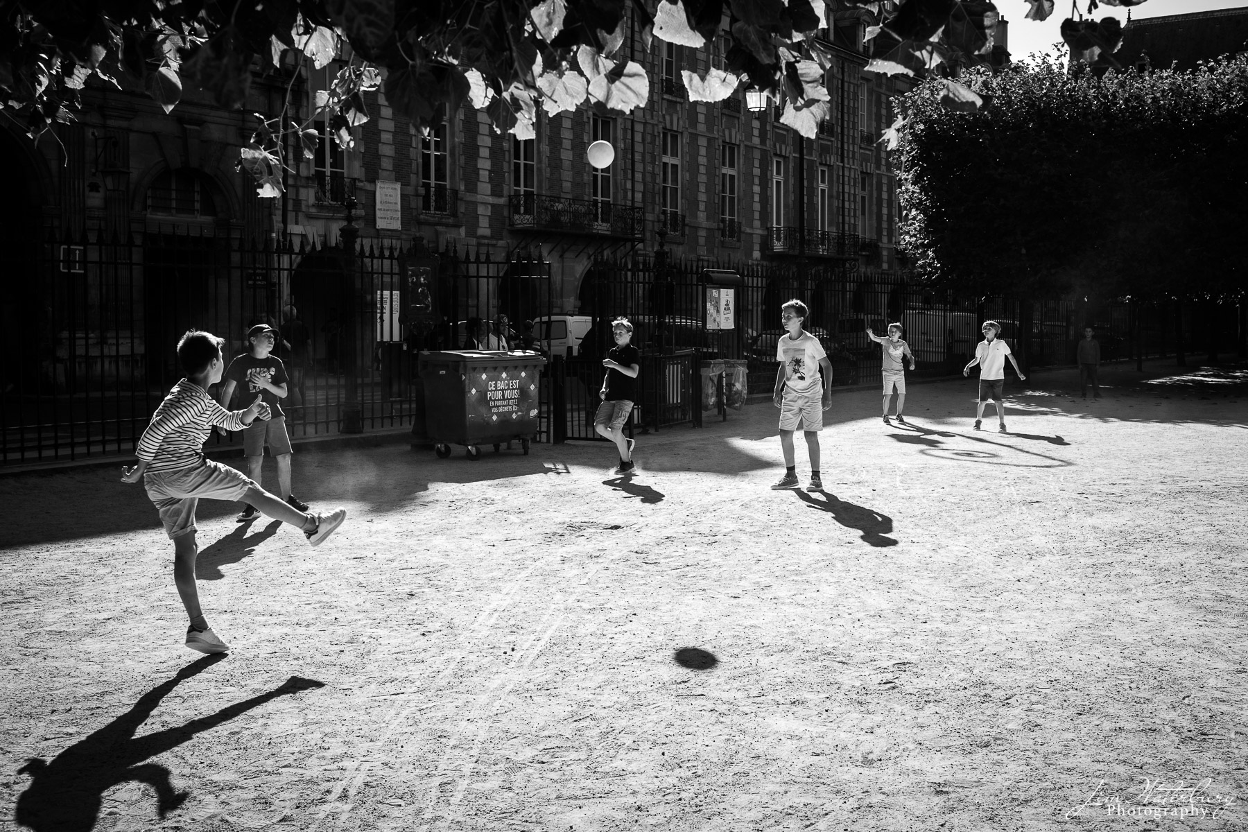 Boys play soccer (football) at the Place des Vosges, Paris, after school. Black & white.