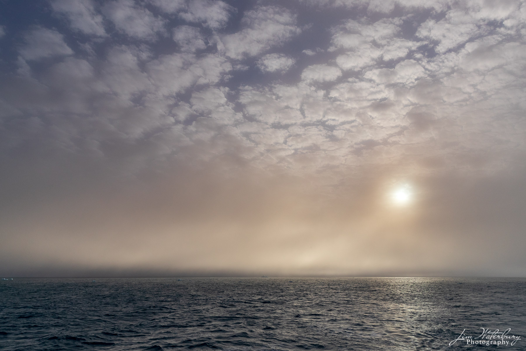 Sun glows through the mist and haze above the waters of the high arctic, near the Austfonna ice cap, Svalbard, Norway.