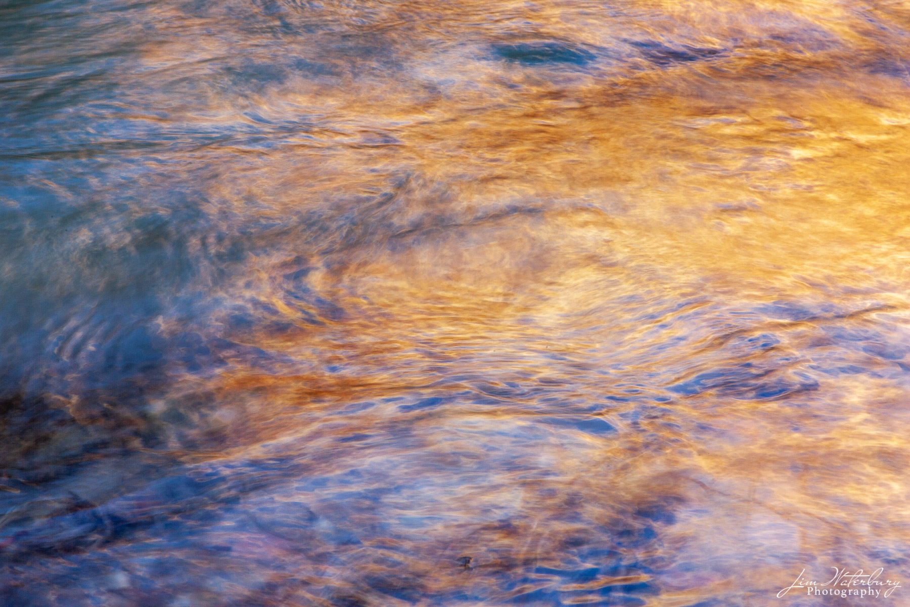Orange and blue light reflects in a stream in Zion National Park.